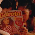 Duas meninas deitadas leem juntas a revista “Toda Garota”, cuja capa traz textos sobre relacionamentos e pré-adolescência.