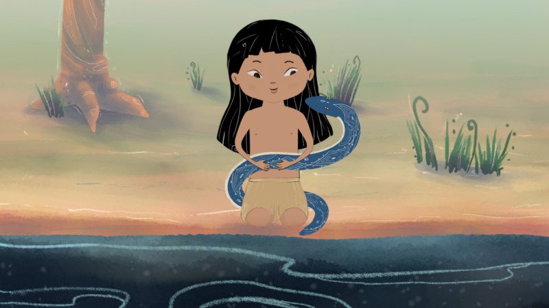 Ilustração de uma criança indígena de cabelos pretos e lisos sentada à beira de um rio, vestindo saia simples de palha e segurando nos braços uma cobra azul com desenhos brancos. Ao fundo há troncos de árvores e vegetação rasteira.