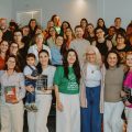 Grupo numeroso de pessoas posa sorridente para foto em ambiente interno; algumas seguram livros e troféus, e há clima de celebração e confraternização.