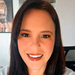 Mulher jovem sorridente, de cabelos longos e escuros, com batom vermelho, em ambiente interno claro.