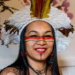 Auritha Tabajara Mulher sorridente com cocar de penas coloridas e pintura indígena no rosto.