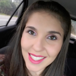 Mulher sorridente de cabelos lisos e castanhos, usando batom rosa, fotografada dentro de um carro.