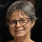 Mulher sorridente de cabelos curtos grisalhos, usando óculos de armação grande.