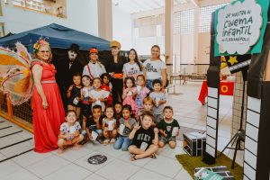 grupo de crianças e educadoras posa sorridente em pátio escolar.