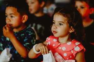 menina de vestido rosa observa atenta enquanto come pipoca.