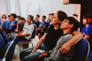 público sentado assiste concentrado a uma exibição em sala.
