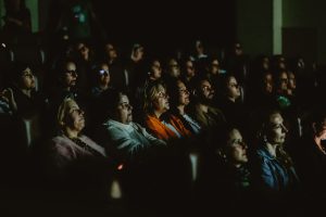 plateia de crianças assiste concentrada em sala escura de cinema.