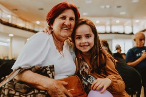 senhora abraça menina de cabelos longos, ambas sorrindo.