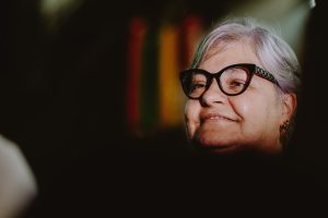 mulher idosa de óculos observa atenta com expressão serena.