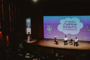 palco com apresentação na Mostra de Cinema Infantil de Florianópolis diante de público em auditório.