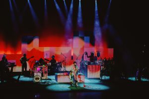 palco iluminado com luzes coloridas durante apresentação musical.