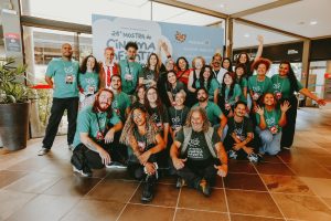 grupo de jovens vestindo camisetas verdes reúne-se para foto coletiva em ambiente iluminado.