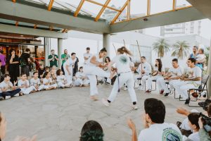 roda de capoeira com crianças e adolescentes vestidos de branco em pátio coberto.