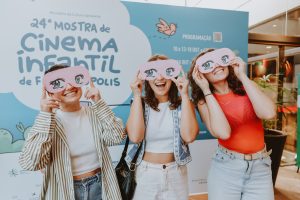 quatro jovens de óculos escuros posam animadas em frente ao painel azul do evento.