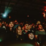 Fotografia de plateia em cinema escuro, com crianças sorrindo e adultos atentos à exibição.