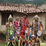 Fotografia de um grupo em trajes folclóricos coloridos diante de uma casa rural.