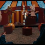 Fotografia de duas crianças assistindo a personagens fantasiados de urso e coelho em um pequeno picadeiro.