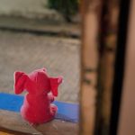 Fotografia de um elefante de pelúcia rosa, visto de costas, sentado no parapeito de uma janela.