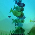 Animação mostra peixes coloridos nadando ao redor de uma grande formação vertical composta por outros peixes.