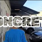 Fotografia de uma criança agachada ao lado de um carro, com a palavra “Concreto” sobreposta em branco.