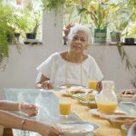 Fotografia de três mulheres e uma menina negras reunidas à mesa do café, em varanda cercada por plantas.
