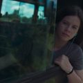 Fotografia de uma menina sentada junto à janela de um ônibus, com o rosto refletido no vidro.