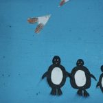 Ilustração artesanal de três pinguins lado a lado sob aves de papel, sobre fundo azul.