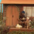 Animação em stop motion mostra personagem diante de uma pequena casa de madeira, cercada por vegetação.