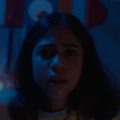 Fotografia em close de uma menina apreensiva, iluminada por luz azul, com pontos coloridos ao fundo.