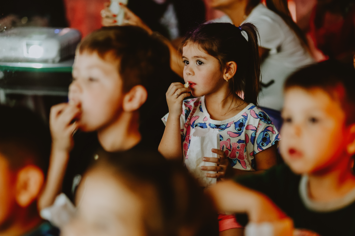 Crianças assistindo atentas à sessão de cinema na escola comendo pipoca.